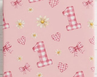 May include: A square sheet of wrapping paper featuring a light pink background with a repeating pattern of white and pink gingham check numbers one, bows, hearts, and small white daisies scattered across the surface.