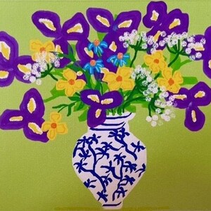 May include: A bouquet of purple irises and yellow flowers in a white vase with a blue and white floral pattern. The vase is sitting on a green background.