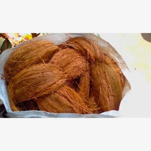 May include: A white bag filled with a large amount of brown coconut fiber. The fiber is long and stringy, and it is tightly packed into the bag.