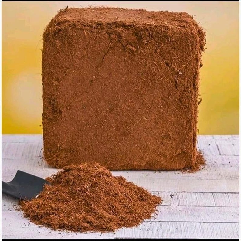 Puede incluir: Un gran ladrillo rectangular de fibra de coco comprimida, de color marr&oacute;n, con un mont&oacute;n de fibra de coco suelta y una peque&ntilde;a paleta negra delante. La fibra de coco es un material natural y fibroso, usado en jardiner&iacute;a.