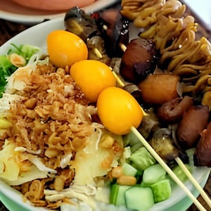 May include: A white bowl filled with a variety of ingredients, including rice, fried onions, and vegetables. Three yellow quail eggs are skewered and placed on top of the bowl. A skewer with various meats and vegetables is placed on the right side of the bowl.
