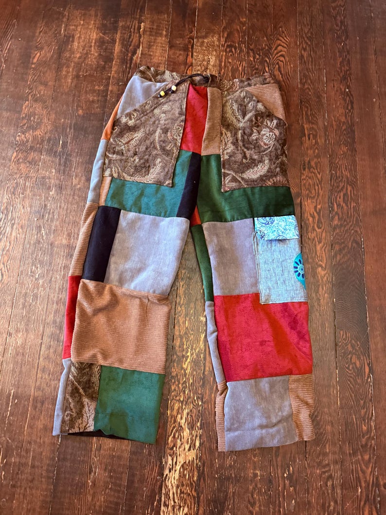 May include: Patchwork pants with a variety of fabrics in shades of brown, green, red, and gray. The pants have a drawstring waist and a loose fit. The design features a mix of textures and patterns, creating a unique and colorful look.