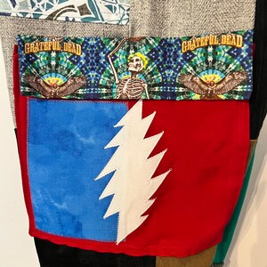 May include: A pair of patchwork pants with a red pocket featuring a white lightning bolt design. The pocket is trimmed with a blue and green fabric with the text "Grateful Dead" printed on it.