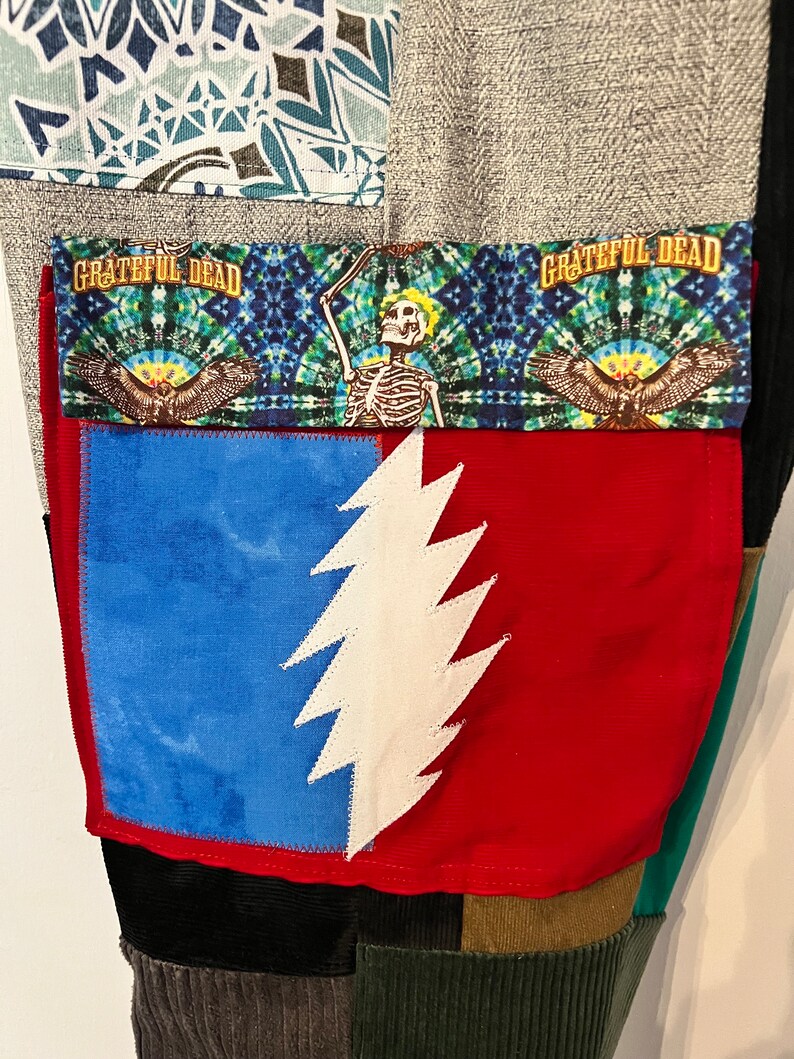 May include: A pair of patchwork pants with a red pocket featuring a white lightning bolt design. The pocket is trimmed with a blue and green fabric with the text "Grateful Dead" printed on it.
