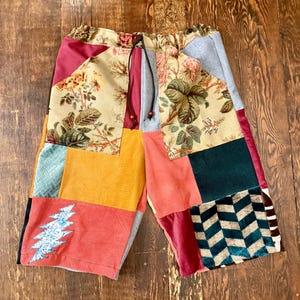 May include: Patchwork shorts with a drawstring waist. The shorts feature a variety of fabrics in different colors and patterns, including floral, corduroy, and geometric designs. The shorts have a relaxed fit and a casual style.