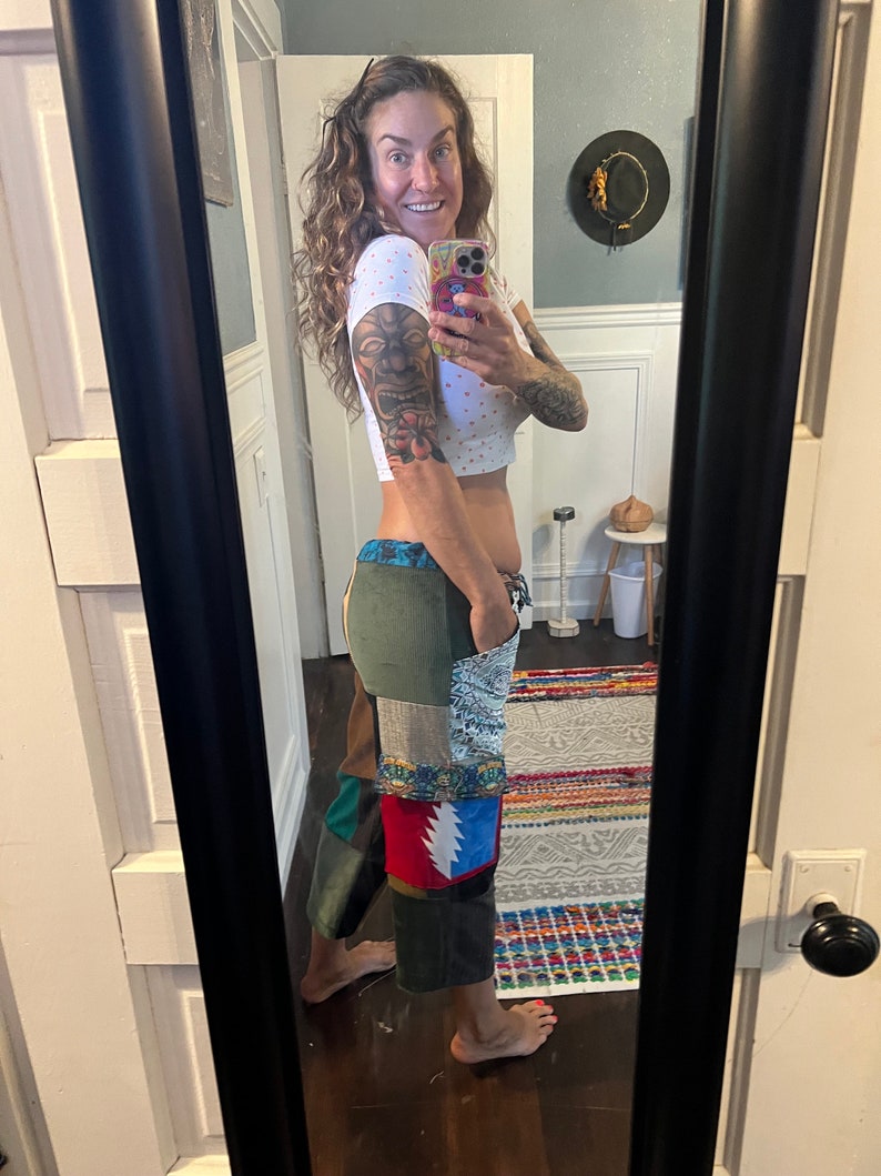 May include: A woman wearing a white crop top with polka dots and patchwork pants. The pants feature a Grateful Dead patch on the left leg. She is standing in front of a mirror and taking a selfie.