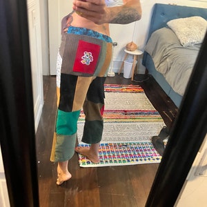 May include: A pair of patchwork pants with a variety of colors and textures, including brown, green, blue, and red. The pants have a large patch on the back with a cartoon bear design.