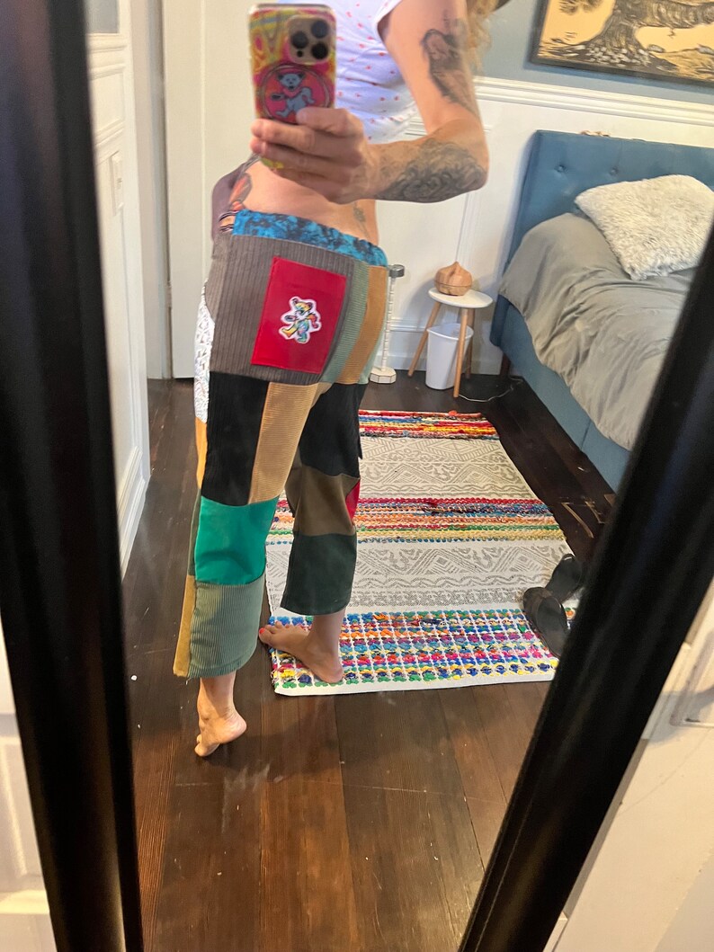 May include: A pair of patchwork pants with a variety of colors and textures, including brown, green, blue, and red. The pants have a large patch on the back with a cartoon bear design.