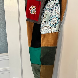 May include: Patchwork pants with a variety of colors and patterns, including brown, green, blue, and red. A small red patch with a colorful bear design is sewn on the front of the pants.