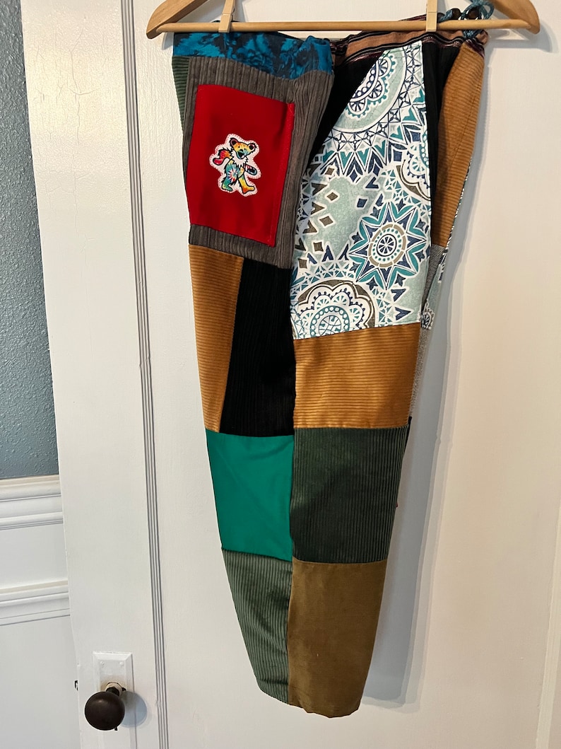May include: Patchwork pants with a variety of colors and patterns, including brown, green, blue, and red. A small red patch with a colorful bear design is sewn on the front of the pants.