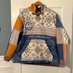 May include: A blue and white patterned hoodie with a yellow and red geometric design. The hoodie has a large pocket on the front with the text "AINTLIFE GRAND" printed on it. There is a small circular patch with the text "AINTLIFE GRAND" on it.