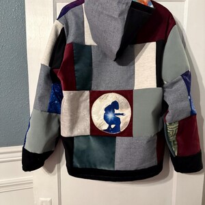 Puede incluir: Una sudadera con capucha de patchwork con una variedad de telas en tonos grises, negros, burdeos y azules. La parte trasera presenta un dise&ntilde;o circular con la silueta de una persona. La sudadera tiene capucha y dobladillo negro.