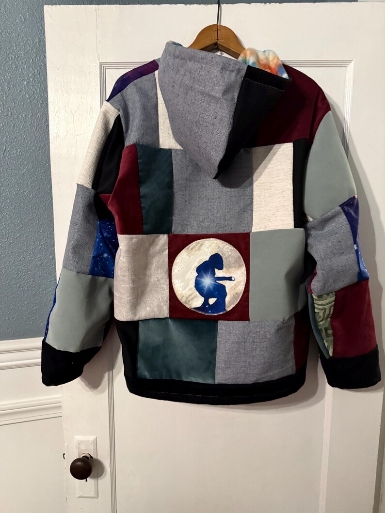 Puede incluir: Una sudadera con capucha de patchwork con una variedad de telas en tonos grises, negros, burdeos y azules. La parte trasera presenta un dise&ntilde;o circular con la silueta de una persona. La sudadera tiene capucha y dobladillo negro.