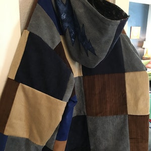 Pode incluir: Uma jaqueta de patchwork com capuz, feita de diferentes tons de veludo cotel&ecirc; marrom, azul e bege. O capuz tem um design de raio.