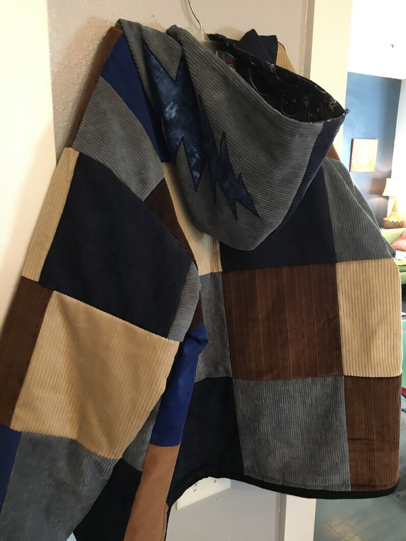 Pode incluir: Uma jaqueta de patchwork com capuz, feita de diferentes tons de veludo cotel&ecirc; marrom, azul e bege. O capuz tem um design de raio.