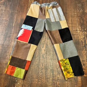 May include: Patchwork pants with a variety of fabric squares in shades of brown, black, gray, and tan. The pants have a floral patterned waistband and a relaxed fit. The patchwork design includes stripes and geometric patterns.