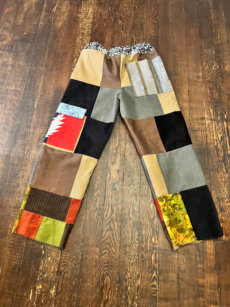 May include: Patchwork pants with a variety of fabric squares in shades of brown, black, gray, and tan. The pants have a floral patterned waistband and a relaxed fit. The patchwork design includes stripes and geometric patterns.