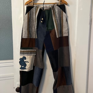 May include: Patchwork pants with a drawstring waist and a variety of colors and textures, including brown, blue, green, and white. The pants have a small embroidered design on the left leg.