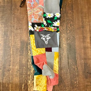 Pu&ograve; includere: Pantaloni patchwork con una variet&agrave; di motivi e colori di tessuto, tra cui paisley, floreali e blocchi a tinta unita. I pantaloni presentano una vita con coulisse e una tasca grigia con una grafica a testa di capra bianca. Il design &egrave; un mix di trame e tonalit&agrave;.