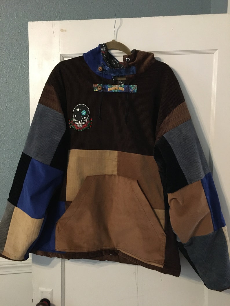 Pode incluir: Uma jaqueta de moletom marrom com capuz de veludo cotel&ecirc; com um design de patchwork. A jaqueta tem um grande bolso na frente e um capuz com cord&atilde;o. A jaqueta &eacute; decorada com um patch Grateful Dead e uma etiqueta "Grateful Dead".
