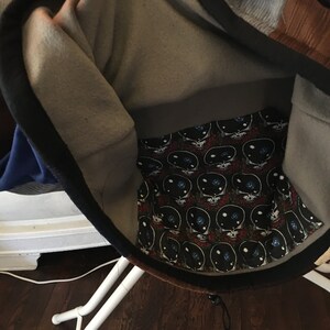 Pode incluir: Uma jaqueta de moletom cinza e marrom com z&iacute;per preto e cord&atilde;o preto. O interior do capuz &eacute; forrado com um tecido preto e branco com um padr&atilde;o repetido de caveiras com olhos e um design de gal&aacute;xia.