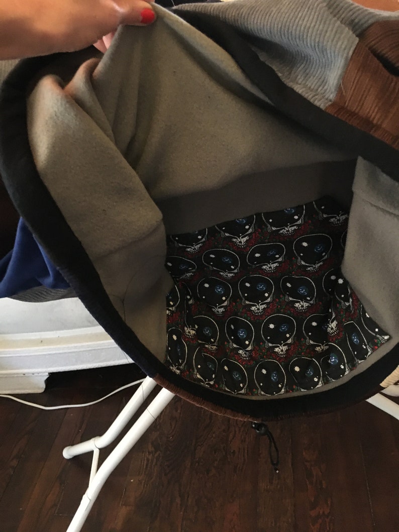 Pode incluir: Uma jaqueta de moletom cinza e marrom com z&iacute;per preto e cord&atilde;o preto. O interior do capuz &eacute; forrado com um tecido preto e branco com um padr&atilde;o repetido de caveiras com olhos e um design de gal&aacute;xia.