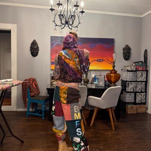 Pu&ograve; includere: Una persona indossa una felpa con cappuccio tie-dye e pantaloni patchwork con le lettere "BMFS" sulla gamba. I pantaloni presentano vari modelli di tessuto, tra cui disegni floreali e geometrici. La persona indossa stivali color cachi.