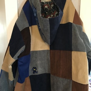 Pode incluir: Uma jaqueta de veludo cotel&ecirc; patchwork com capuz. A jaqueta &eacute; feita de diferentes cores de veludo cotel&ecirc;, incluindo marrom, azul e bege. O capuz &eacute; forrado com um tecido com um padr&atilde;o de caveira e ossos cruzados. H&aacute; um pequeno urso bordado na frente da jaqueta.