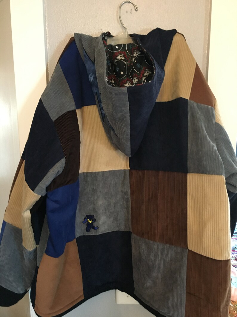 Pode incluir: Uma jaqueta de veludo cotel&ecirc; patchwork com capuz. A jaqueta &eacute; feita de diferentes cores de veludo cotel&ecirc;, incluindo marrom, azul e bege. O capuz &eacute; forrado com um tecido com um padr&atilde;o de caveira e ossos cruzados. H&aacute; um pequeno urso bordado na frente da jaqueta.