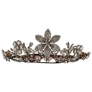 May include: An antique tiara with a floral design. The tiara features a large flower in the centre and smaller flowers on the sides, all encrusted with sparkling gemstones. The metalwork has a vintage, tarnished appearance.