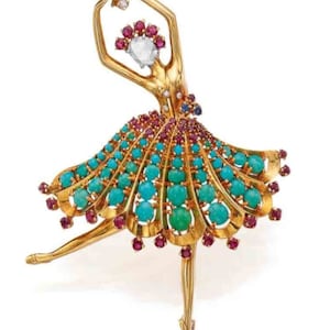 May include: A gold ballerina brooch featuring a turquoise and ruby skirt. The dancer's arms are raised, holding a diamond. The skirt is decorated with turquoise cabochons and ruby accents, creating a vibrant and elegant design.