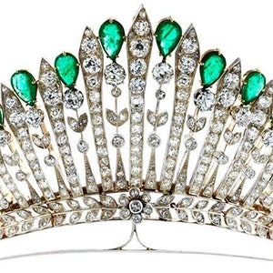 May include: A detailed tiara with a fan-shaped design, adorned with emerald-green gemstones and sparkling diamonds. The tiara is crafted from silver and gold metalwork, incorporating floral and leaf motifs, presenting a luxurious and elegant aesthetic.