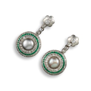 May include: A pair of drop earrings with a circular design. Each earring has a central pearl, encircled by emeralds and diamonds. A flower-shaped element with a diamond centre tops each earring, connected by a line of diamonds.