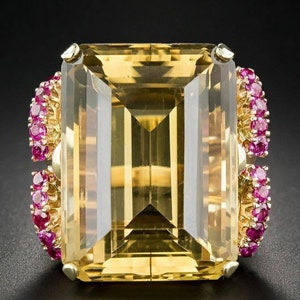 May include: A large, rectangular yellow gemstone ring with a gold band. The ring is flanked by two clusters of small, round pink gemstones. The ring's central stone is faceted, reflecting light. The setting is gold-colored.