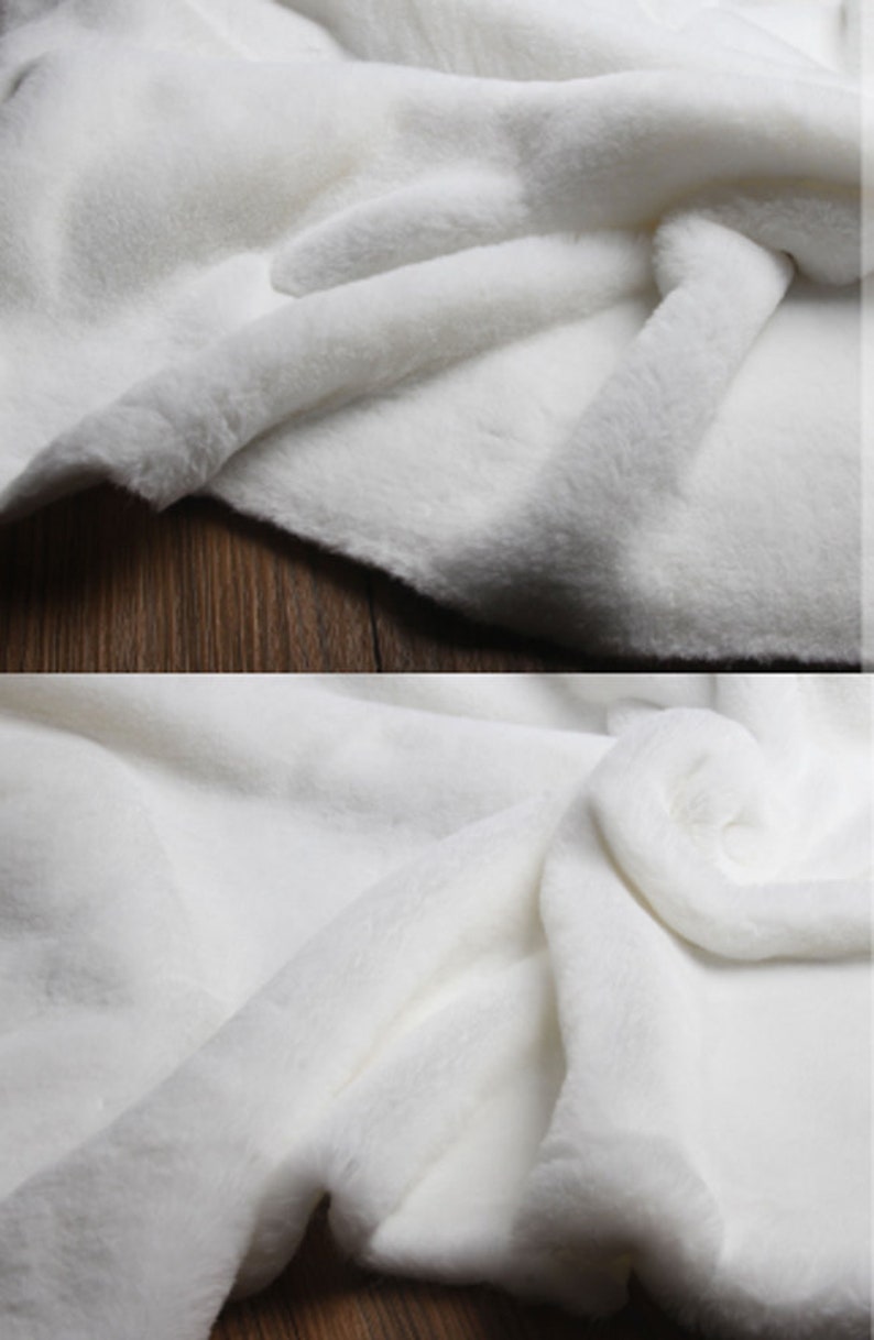 May include: White faux fur fabric with a soft, plush texture. The fabric is folded and draped, showcasing its luxurious feel.