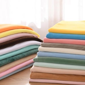 May include: A collection of stacked fabric pieces in a range of colours, such as yellow, orange, pink, brown, white, teal, and blue. The fabric has a soft, velvety appearance. The neatly arranged stacks suggest a fabric shop or a craft supply store, with a variety of textiles.