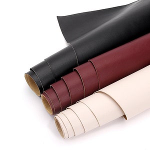 Può includere: Tre rotoli di pelle sintetica in nero, bordeaux e bianco avorio. I rotoli sono impilati uno sopra l'altro.