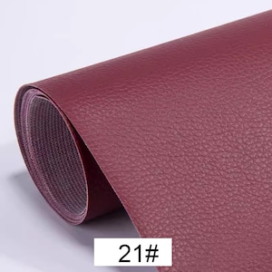 May include: A close-up of a roll of burgundy faux leather fabric with a textured surface. The fabric is rolled up and the edge is visible. The text "21#" is printed on the fabric.