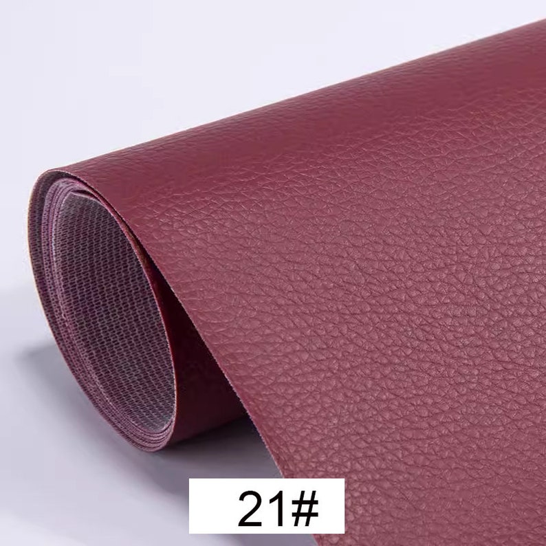 May include: A close-up of a roll of burgundy faux leather fabric with a textured surface. The fabric is rolled up and the edge is visible. The text "21#" is printed on the fabric.