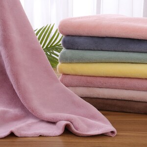 May include: A stack of soft, plush fabric in various pastel colors, including pink, yellow, blue, and green. The fabric is folded neatly and arranged in a pile.