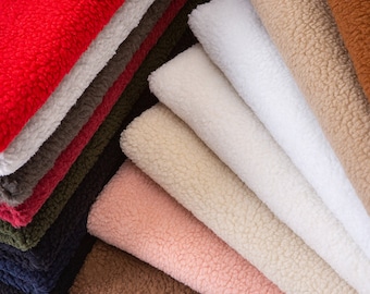 May include: A variety of plush fabrics in different colors, including red, white, brown, beige, and pink. The fabrics are folded and stacked on top of each other, creating a soft and inviting texture.