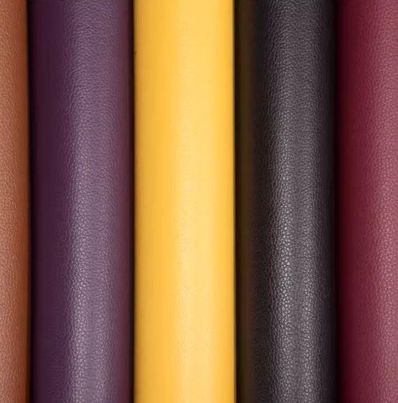 May include: Close-up of five different colored rolls of faux leather. The colors are brown, purple, yellow, black, and burgundy.