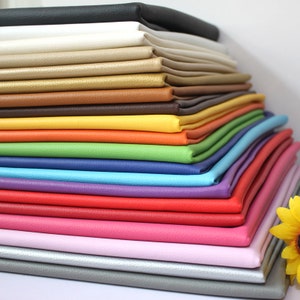 May include: A stack of 18 different colored faux leather fabric swatches. The colors include black, white, beige, gold, brown, yellow, orange, green, blue, purple, red, pink, light pink, gray, and silver.