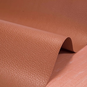 May include: Close-up of a textured, brown leather fabric. The fabric has a subtle, pebbled texture.