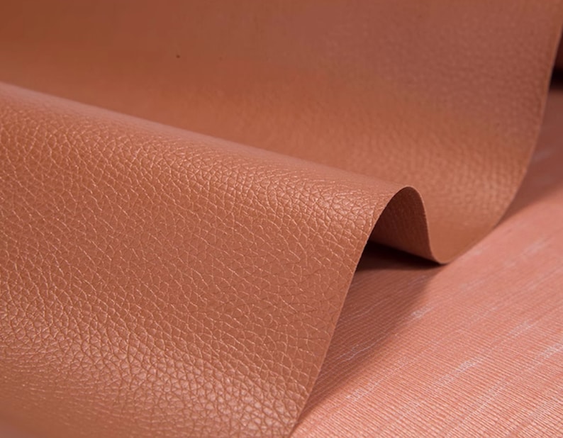 May include: Close-up of a textured, brown leather fabric. The fabric has a subtle, pebbled texture.