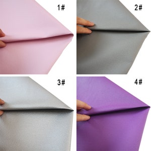 May include: Four samples of faux leather in different colors: pink, gray, silver, and purple. Each sample is folded in half and held by a hand.