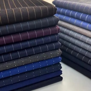 May include: A stack of fabric swatches in various colors and patterns, including stripes and polka dots. The swatches are arranged in a neat pile, with the top swatch being a black fabric with thin gold stripes.