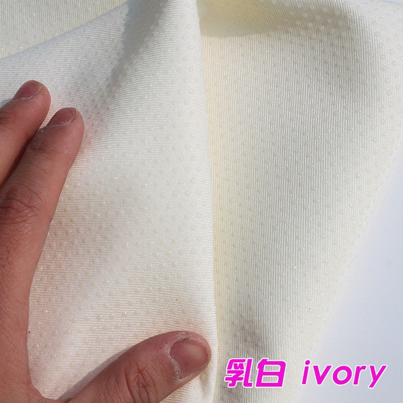 May include: Close-up of a soft, ivory-colored fabric with a textured, dotted pattern. The fabric is folded in half, revealing the underside of the material.