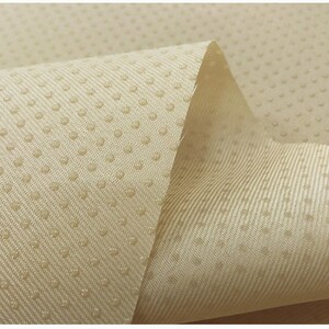 May include: Close-up of a beige fabric with a textured surface. The fabric has a pattern of small dots.