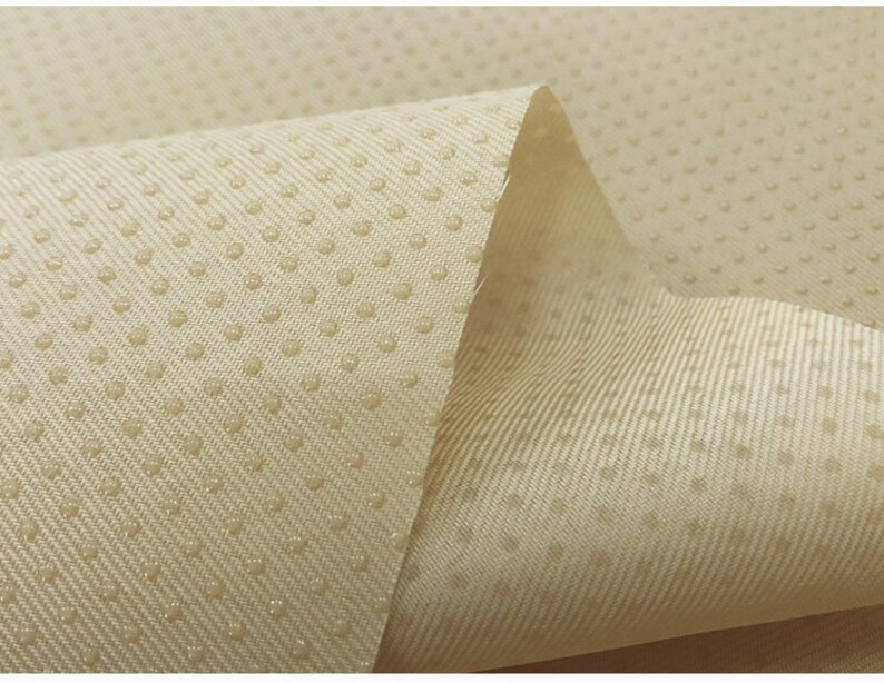 May include: Close-up of a beige fabric with a textured surface. The fabric has a pattern of small dots.